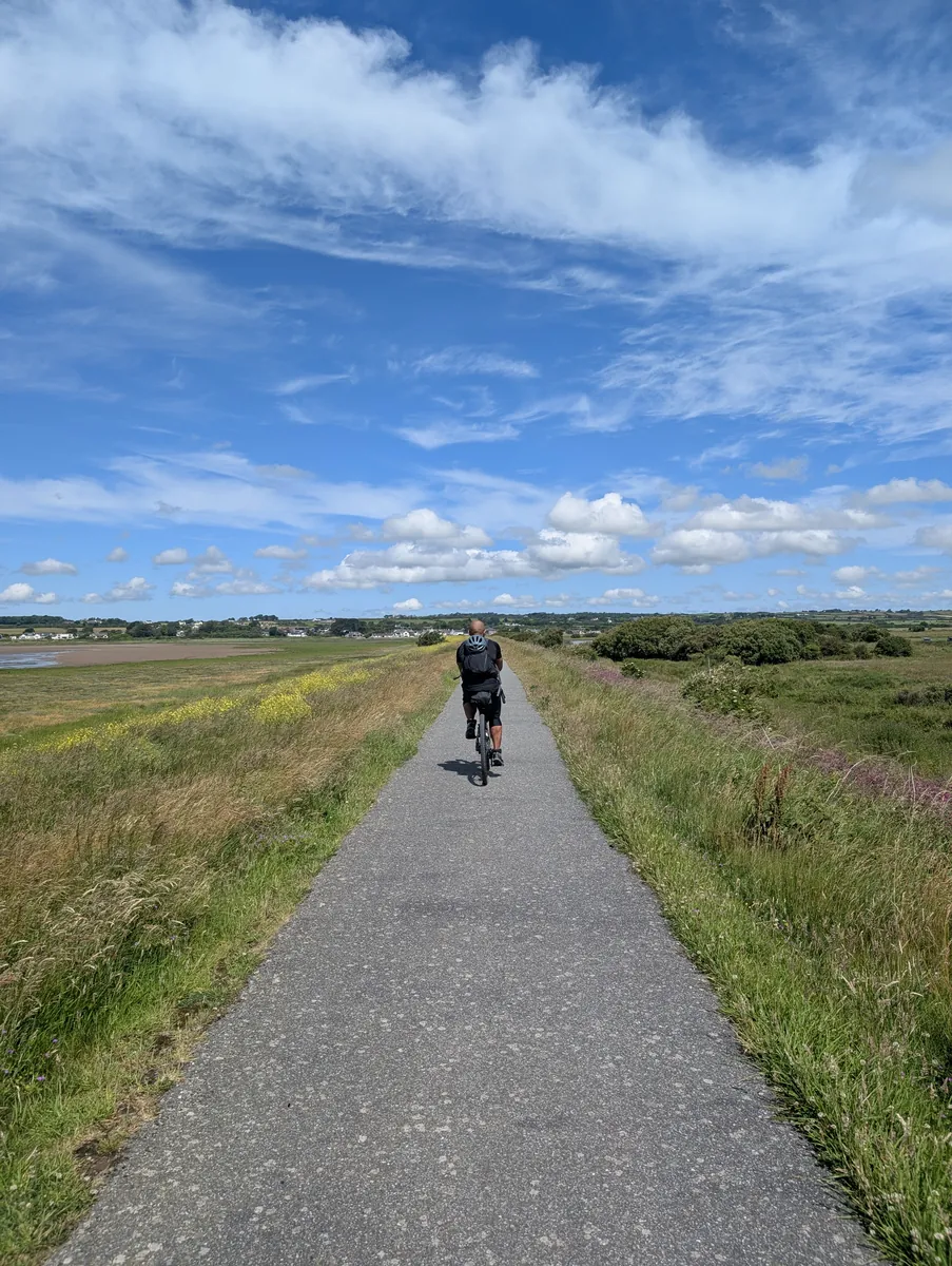 A rider seen from behind on a long path under a big sky