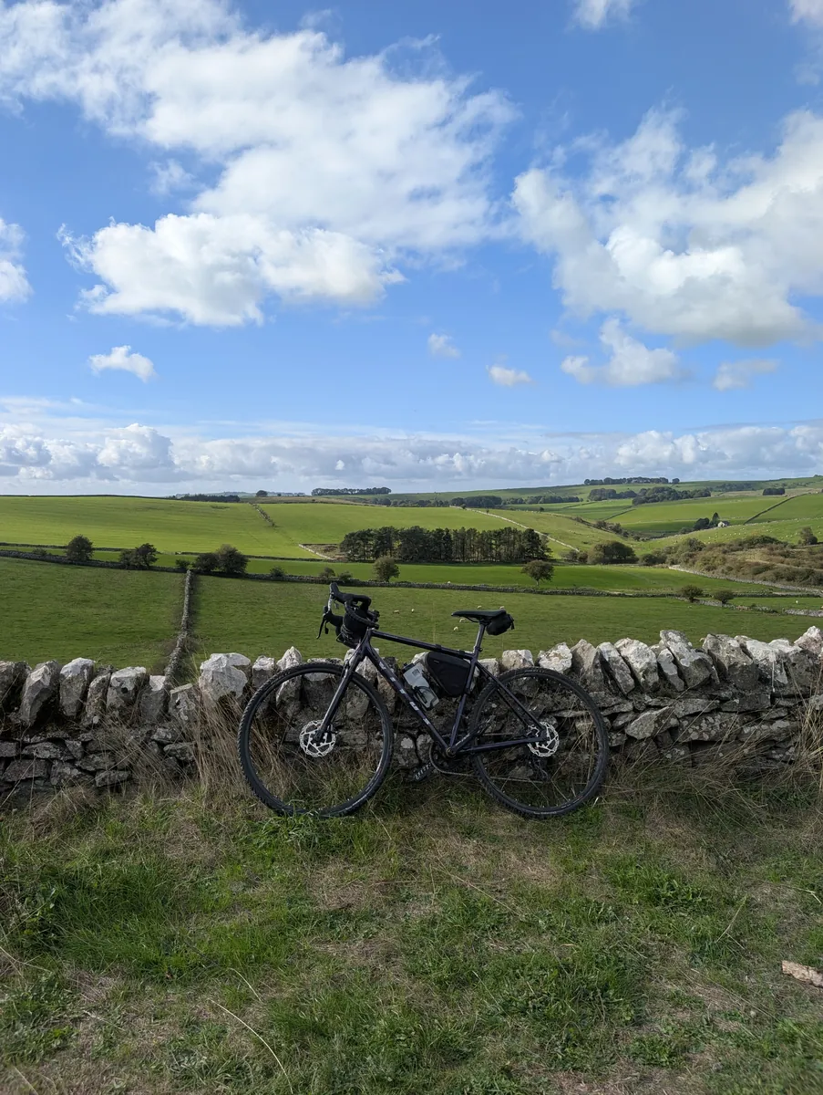 A bike leaning on a dry stone wall above green fields